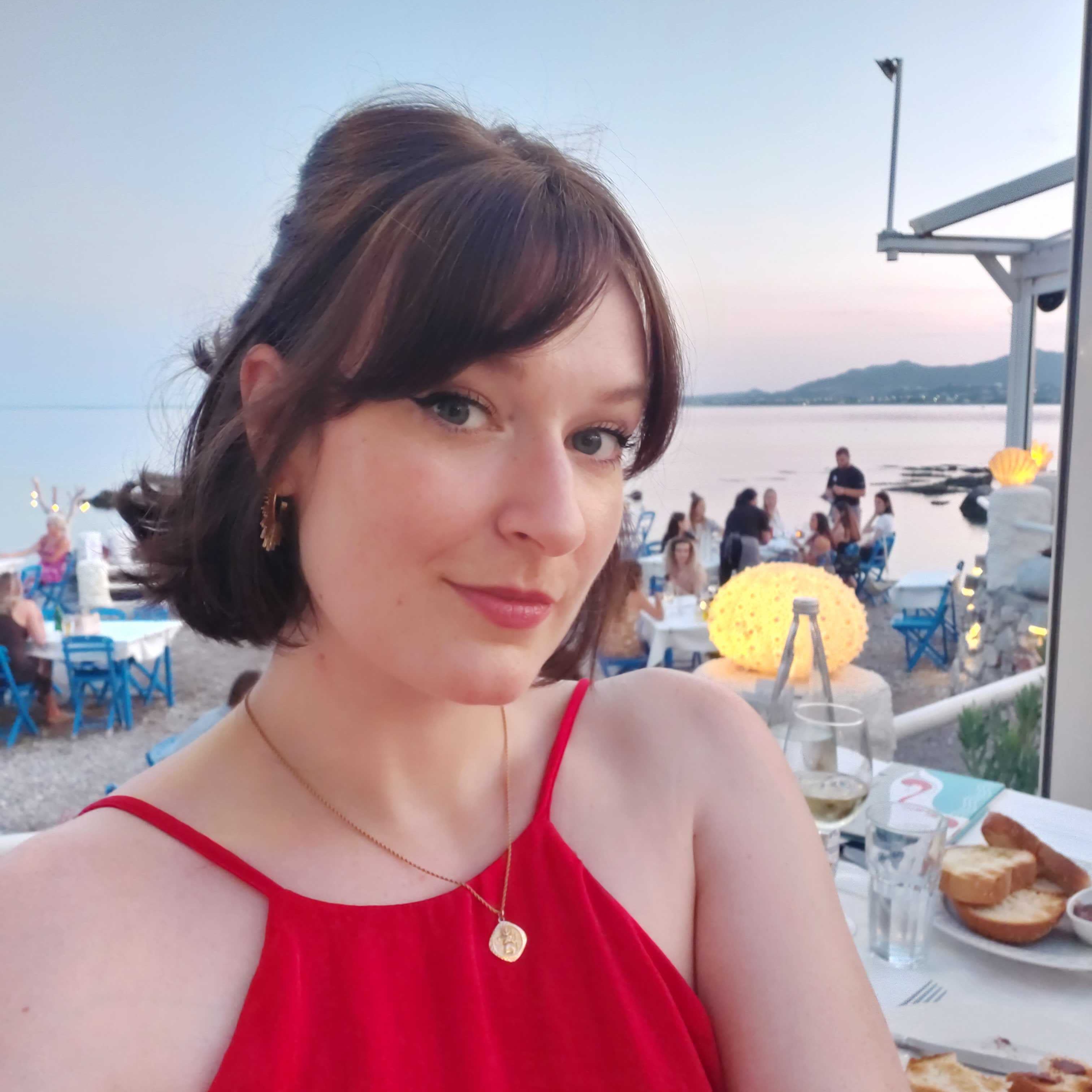 Woman in a red dress sitting at an outdoor table with a scenic background